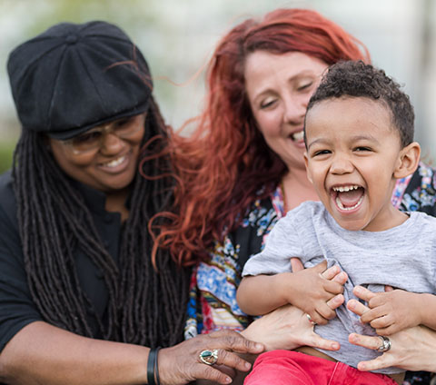 Two mothers smiling and holding their child.